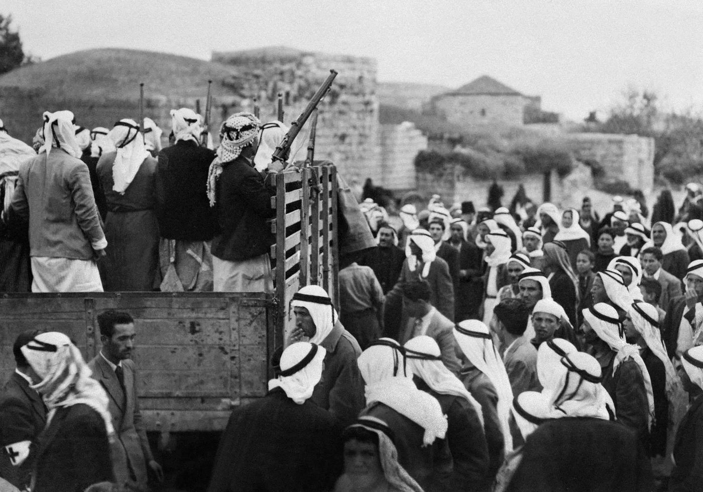 Armed Arab fighters standing in a truck with rifles, surrounded by a large crowd, during the 1948 war.